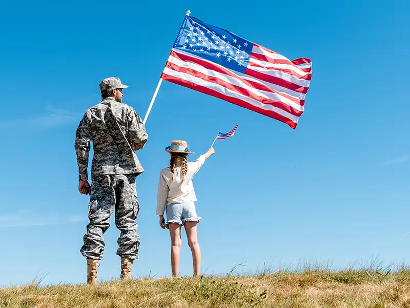 Military man holding American flag with daughter